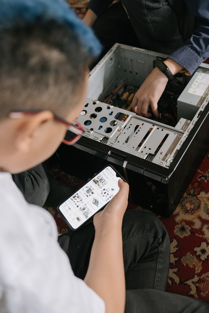 Two individuals fixing a computer while using a smartphone for repair guidance.